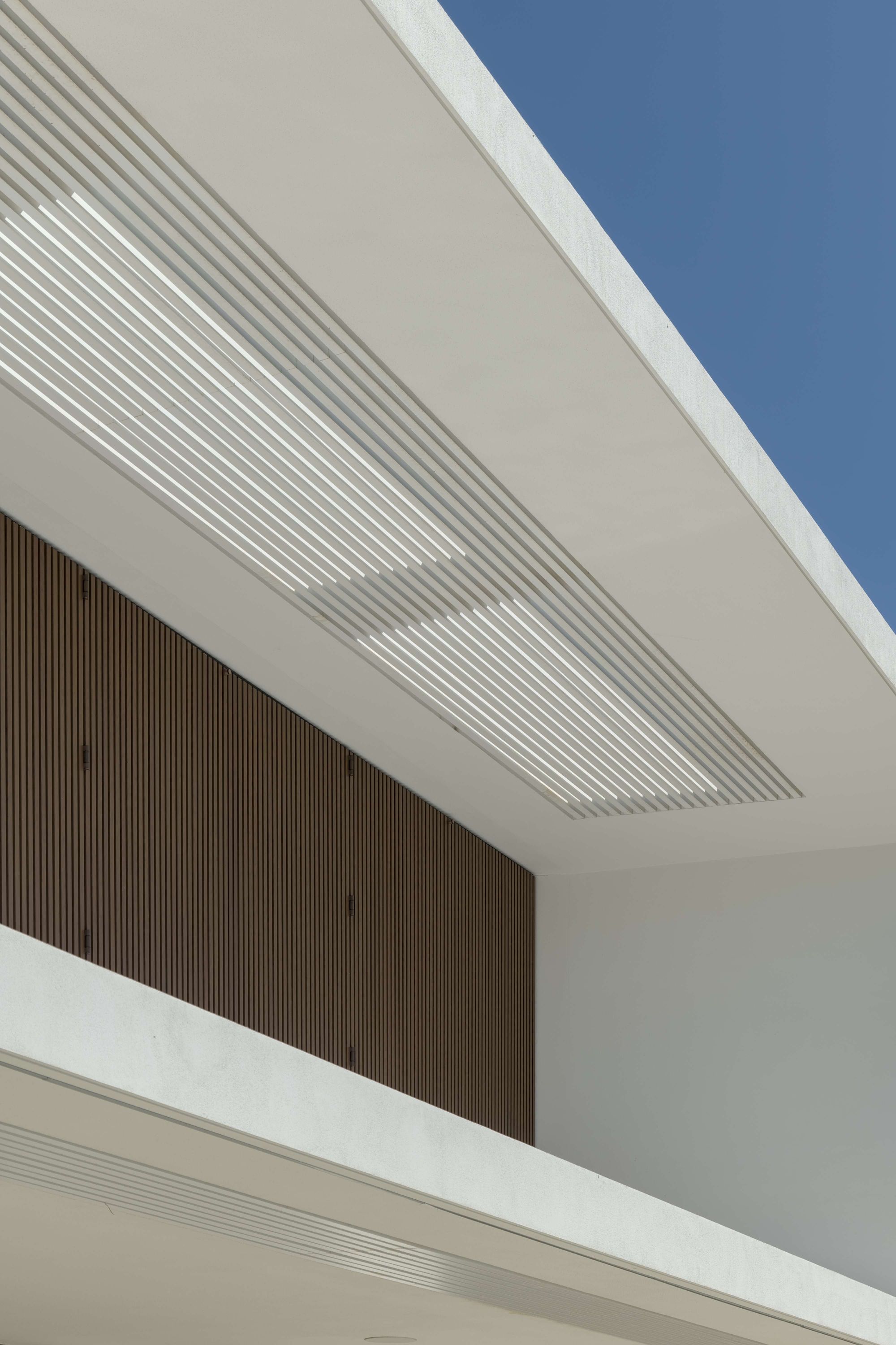 Pormenor da fachada de uma casa contemporânea onde se destaca um gradeamento metálico com textura de madeira