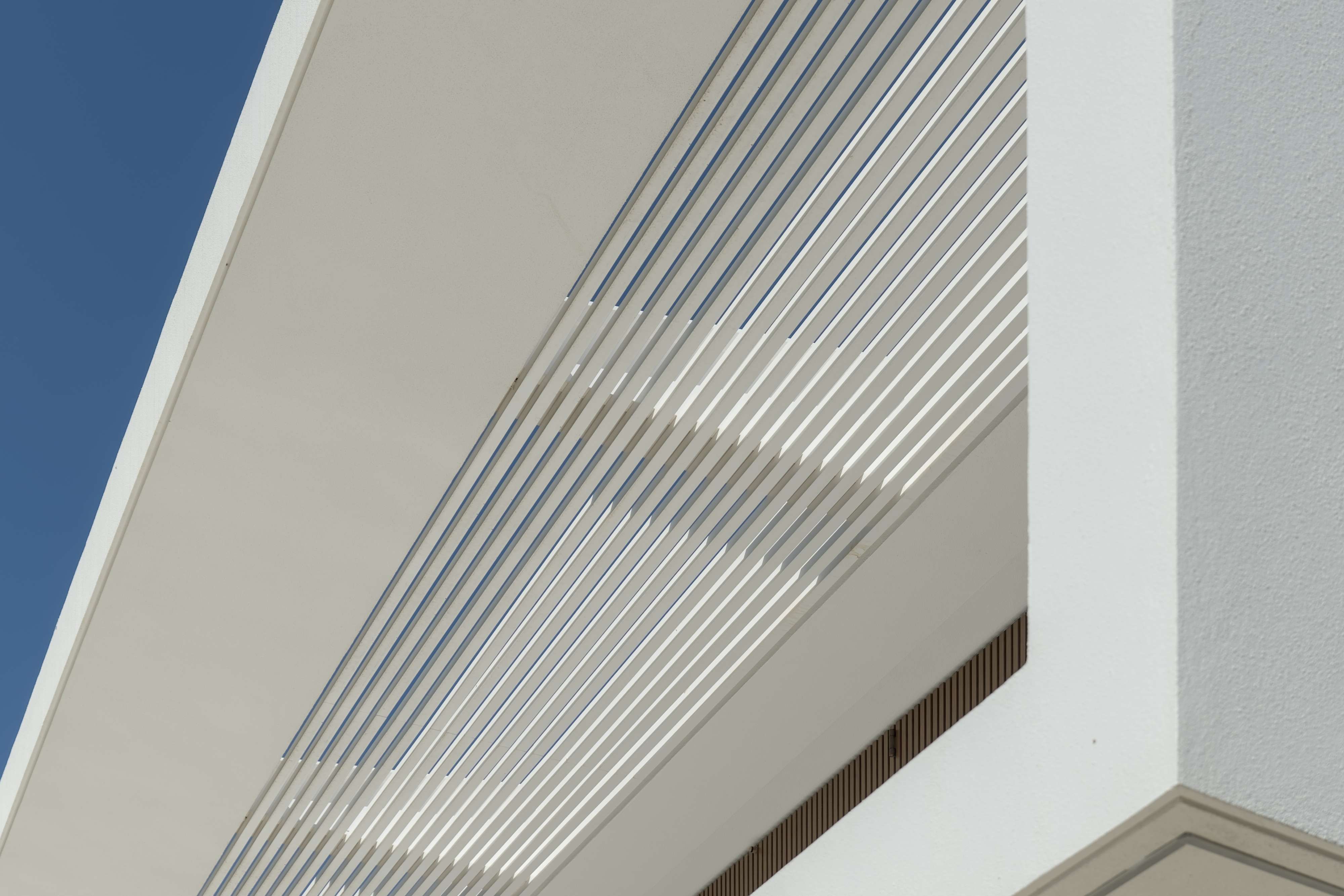 Pormenor da fachada de uma casa contemporânea onde se destaca um gradeamento metálico no teto que permite a passagem de luz de forma controlada.