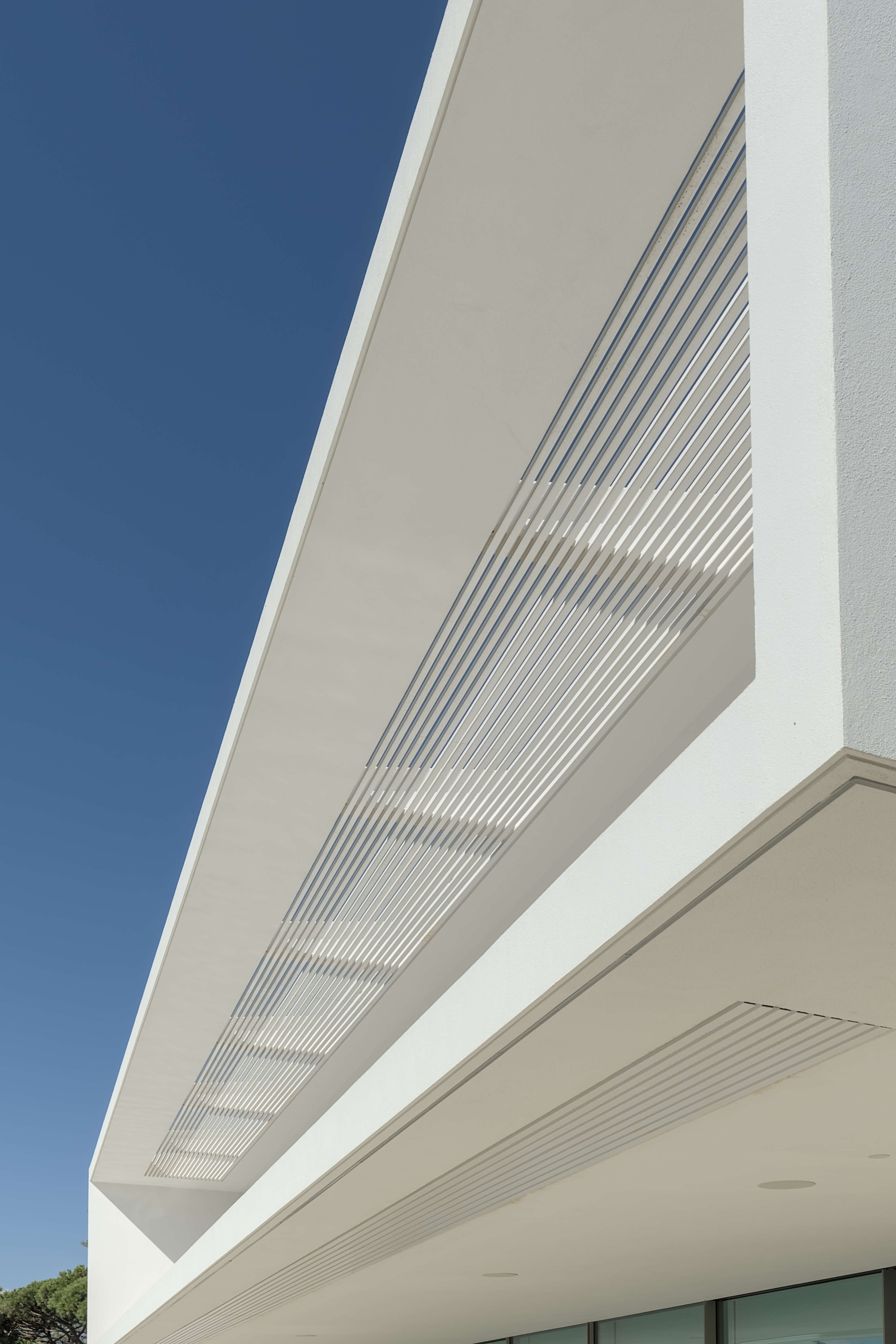 Pormenor da fachada de uma casa contemporânea onde se destaca um gradeamento metálico no teto que permite a passagem de luz de forma controlada.