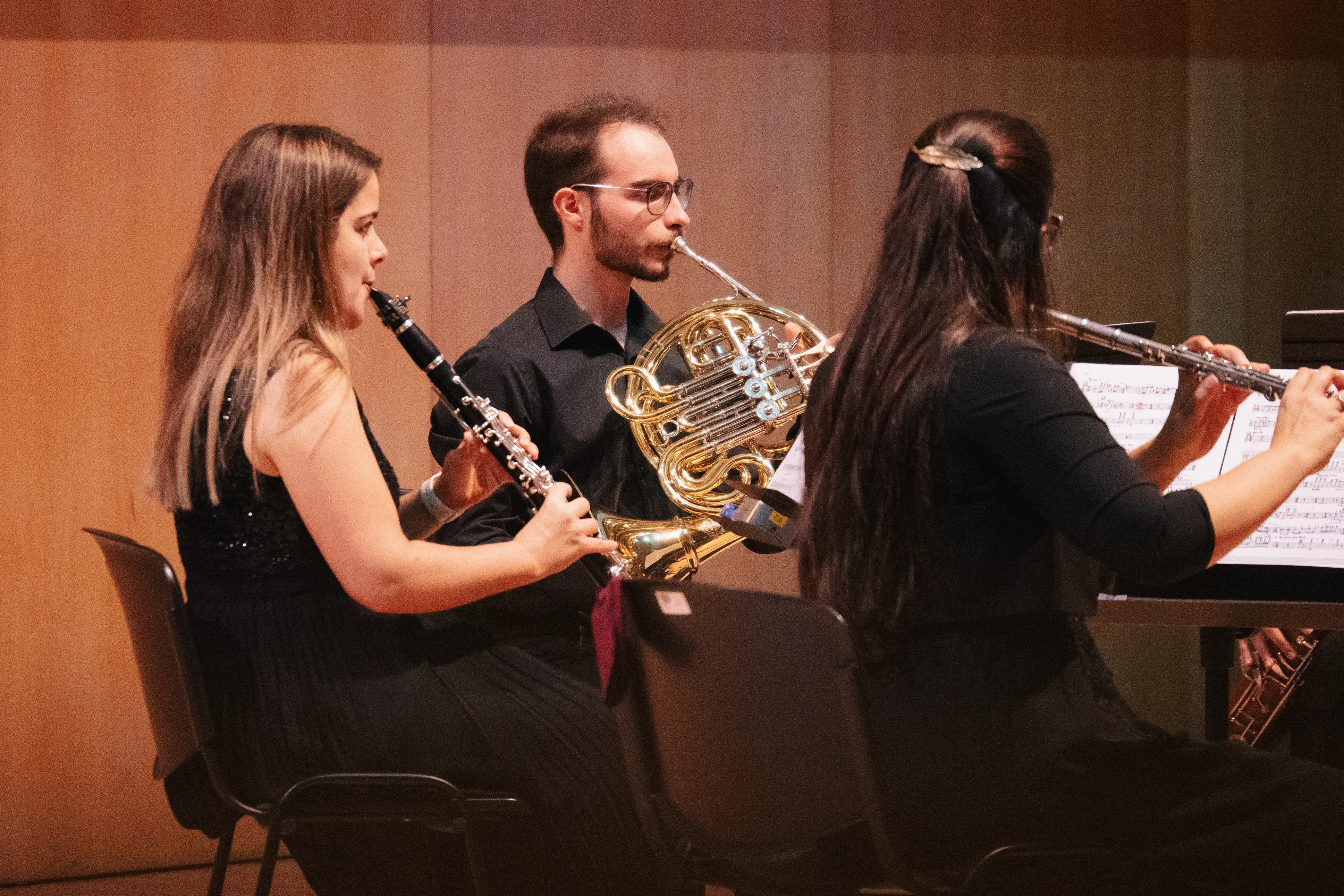 Três músicos tocam instrumentos de sopro num palco.