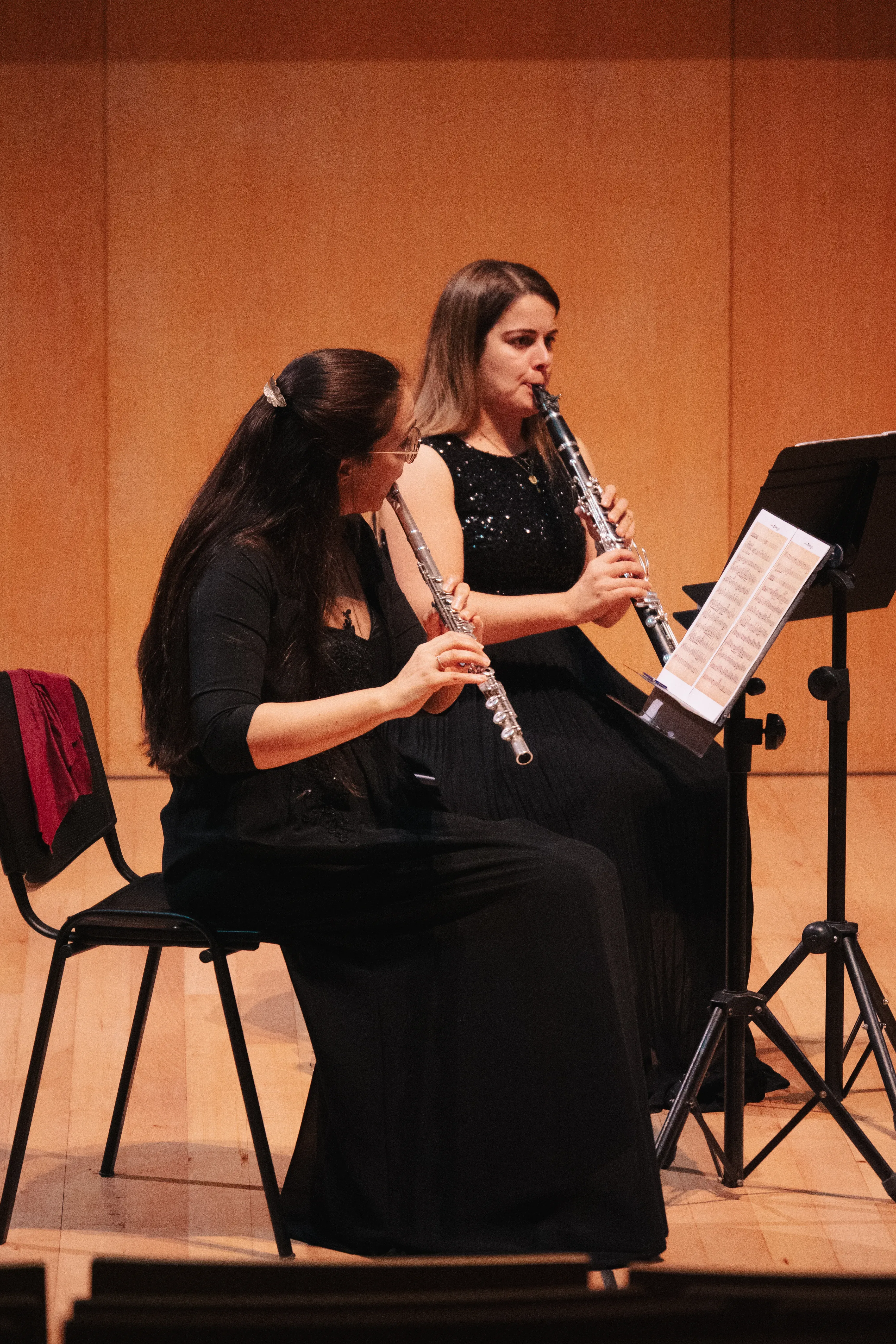 Duas performers tocam instrumentos de sopro num palco.
